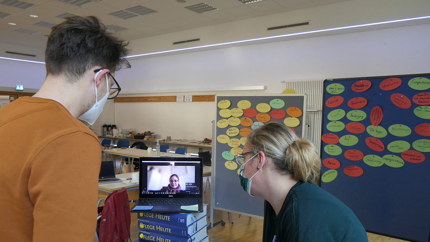 Schulungssituation Digitale Akademie Pflege 4.0 - 2 Personen von hinten, die auf einen Laptop schauen der auf einem Buch steht