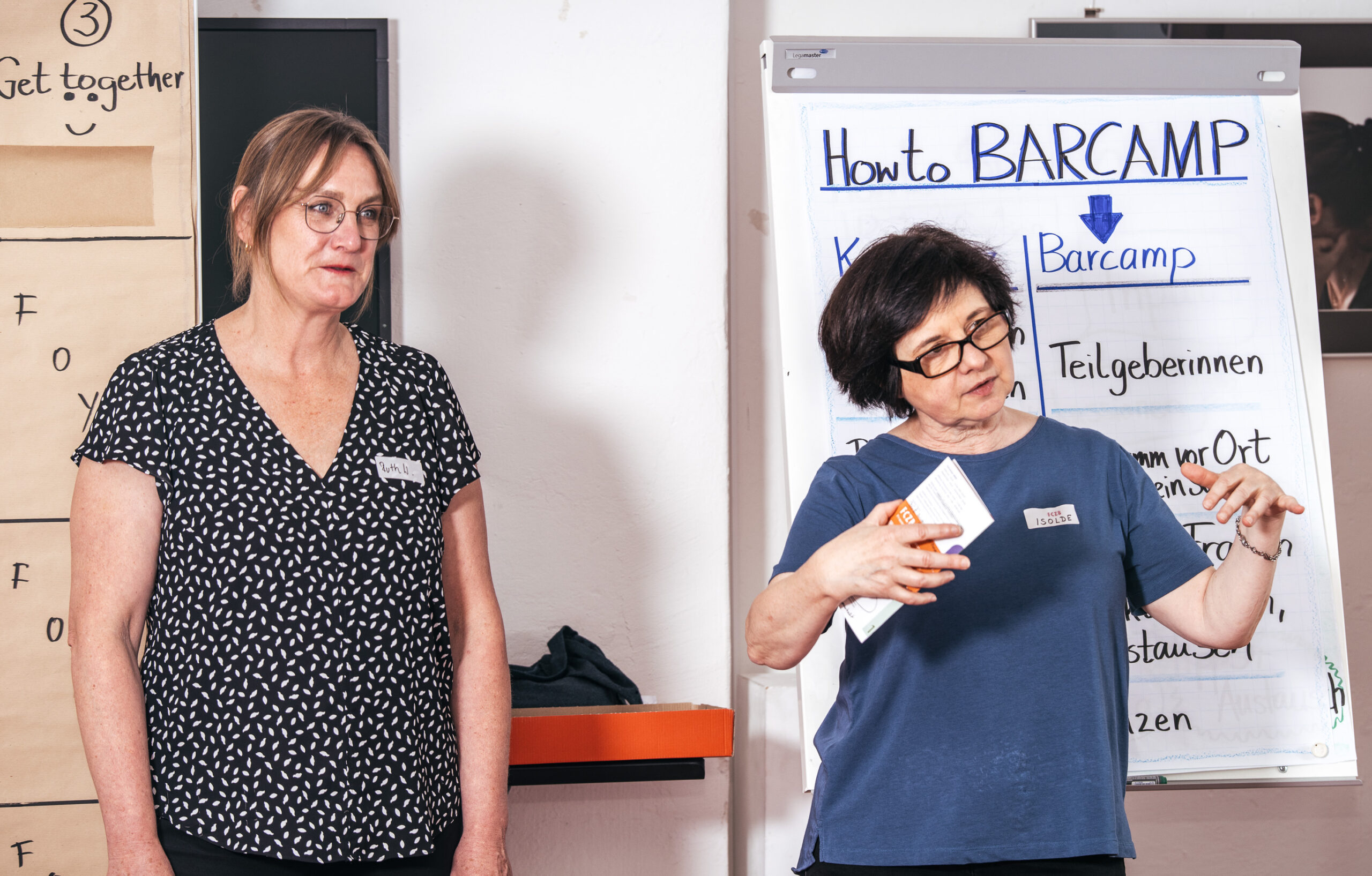 Foto: 2 Mitarbeiterinnen des FCZBstehen vor einem Flipchart mit der Überschrift Barcamp und moderieren das F3 FrauenFinanzBarcamp am 31.5.24 im FCZB an. Copyright: Browse Studios, Foto: Sabine Drwenzki