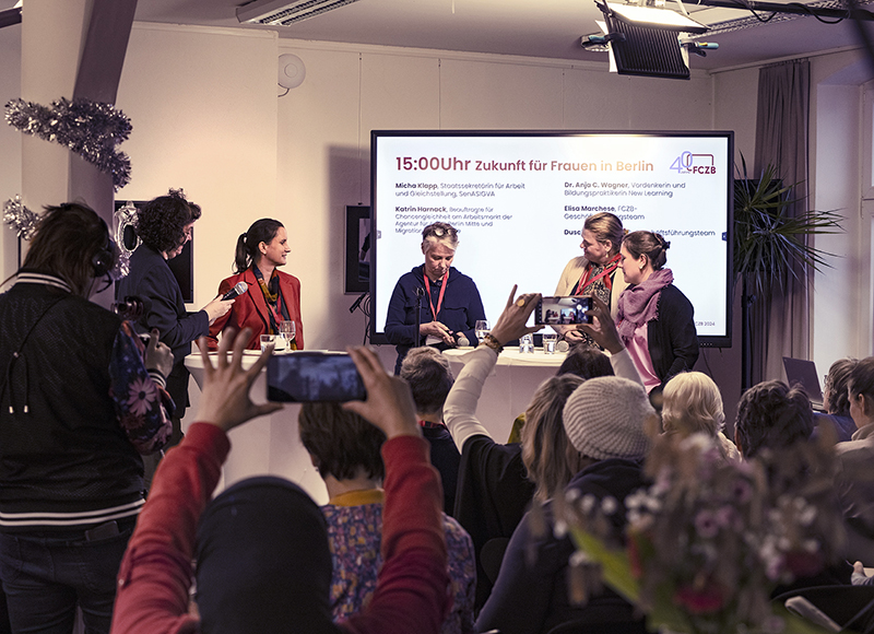 Farbfoto Fachveranstaltung 40 Jahre FCZB, Sprecherinnen-Podium und Publikum, einige halten ihre Handys hoch und fotografieren